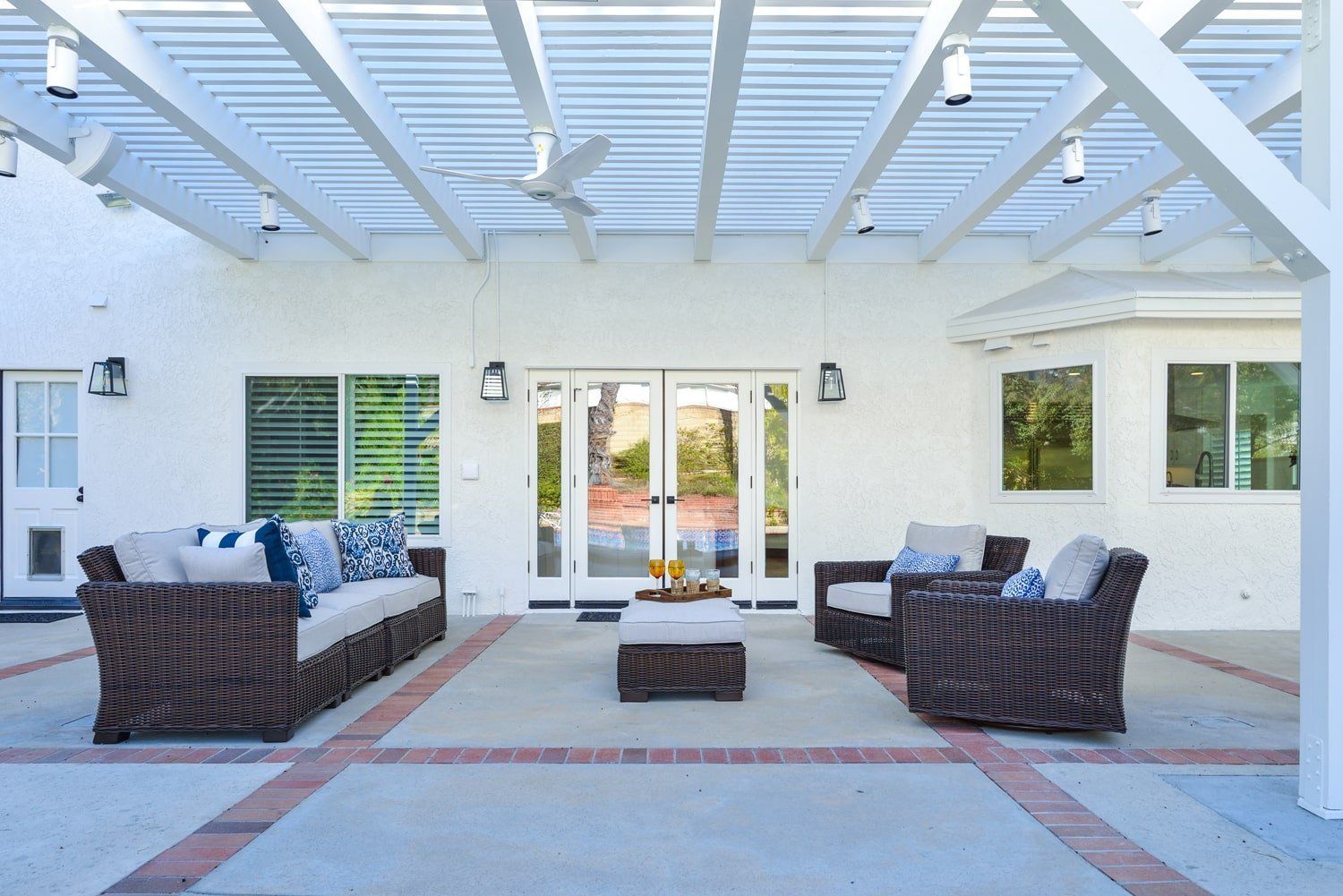 Covered patio with wicker seating, blue cushions, and glass doors beneath a white pergola.