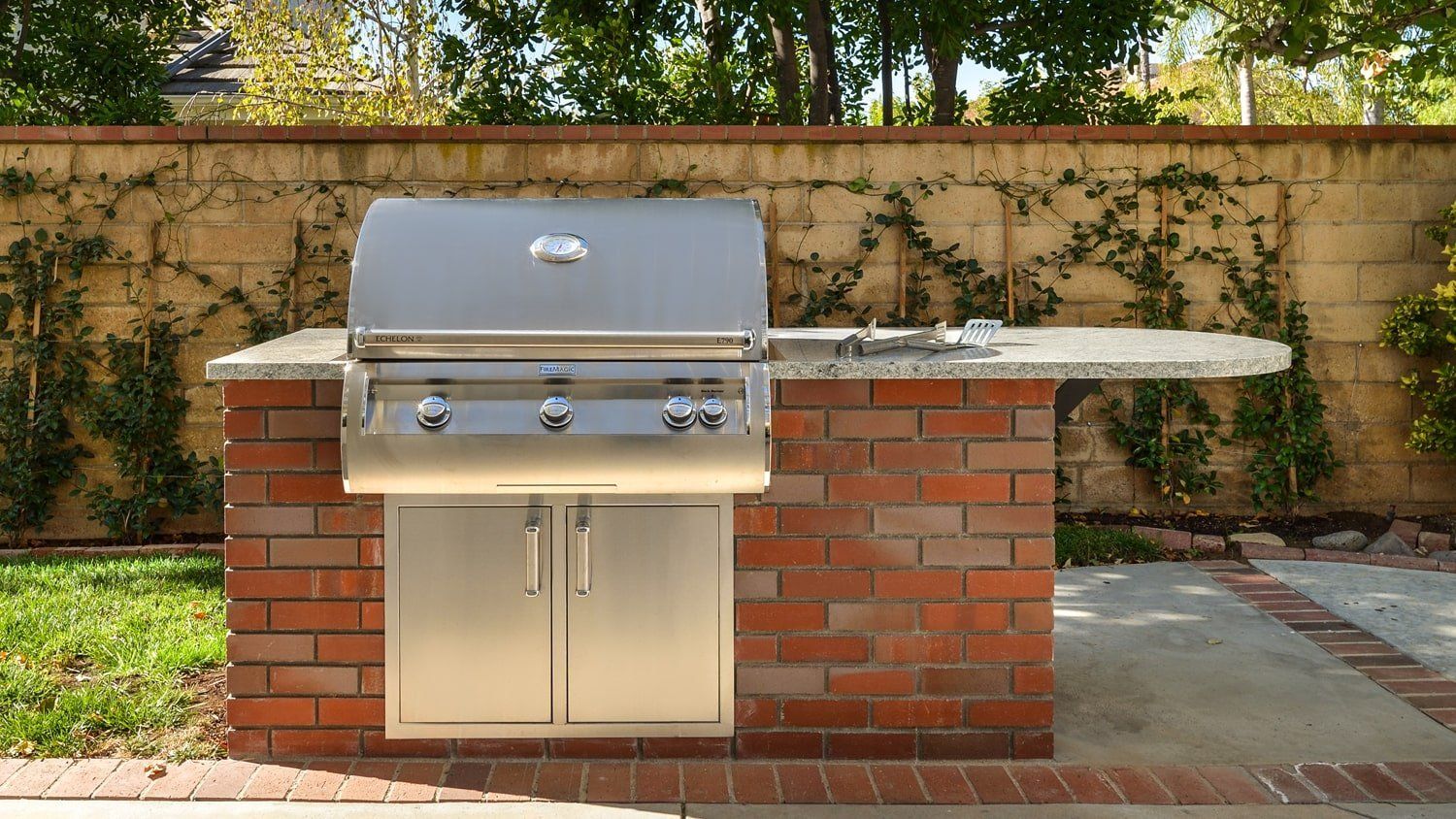 Outdoor brick barbecue grill with stainless steel hood in a backyard patio area
