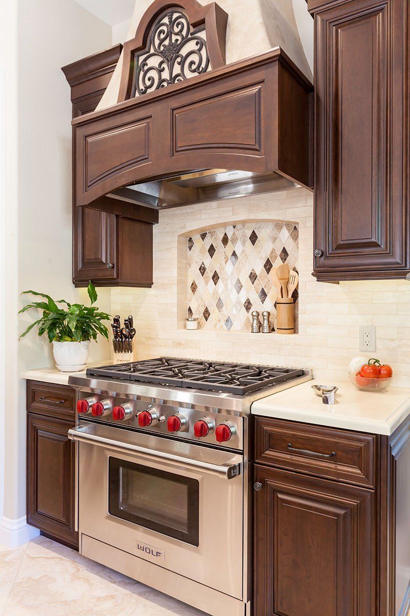 Dark wood kitchen with stainless steel range, ornate hood, and cream tile backsplash