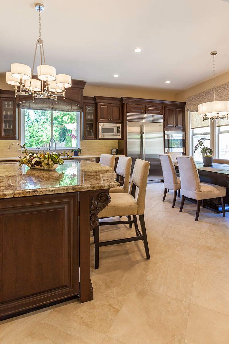 Bright kitchen with dark wood cabinets, granite island, dining table, and stainless-steel refrigerator