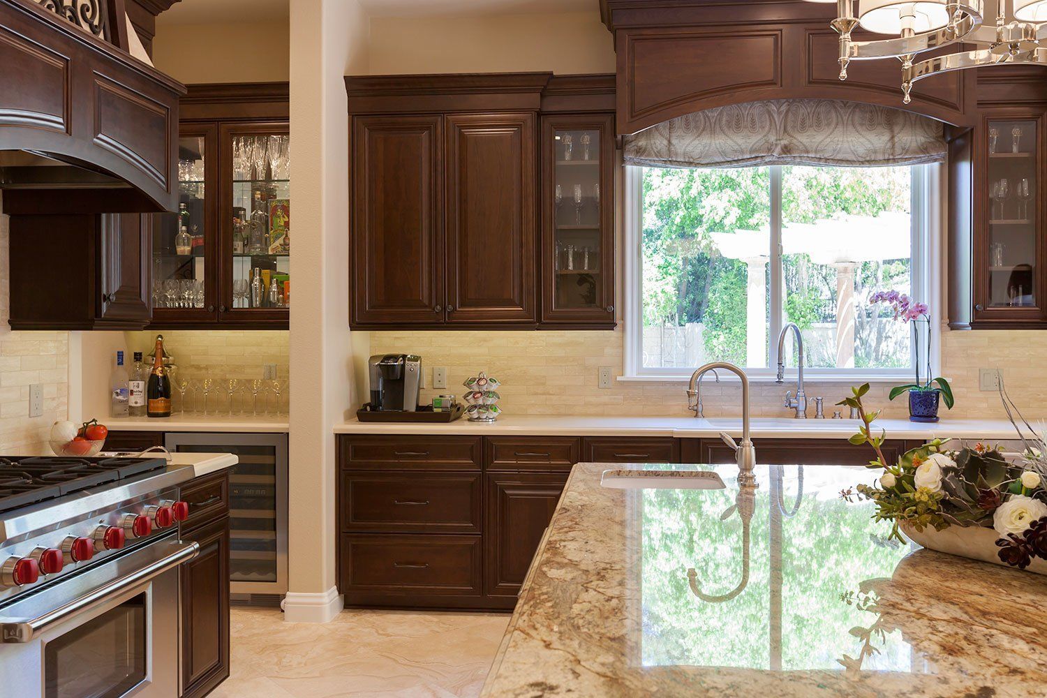 Modern kitchen with dark wood cabinets, stainless stove, and island beneath a large window with greenery outside