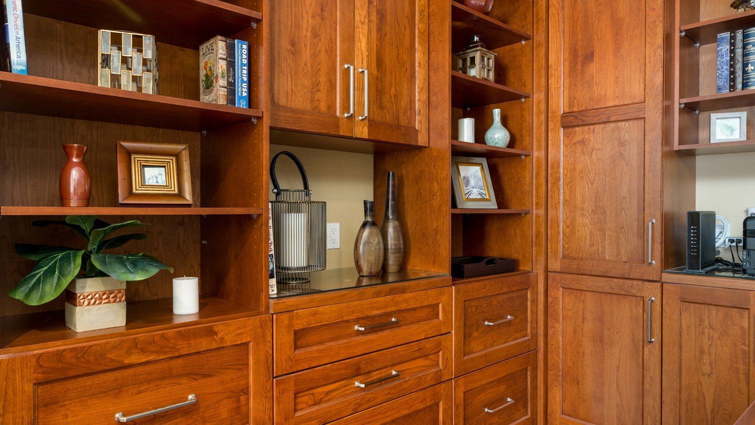 Wooden built-in shelves with books, decor, and a glass cabinet in a warm-toned living room.
