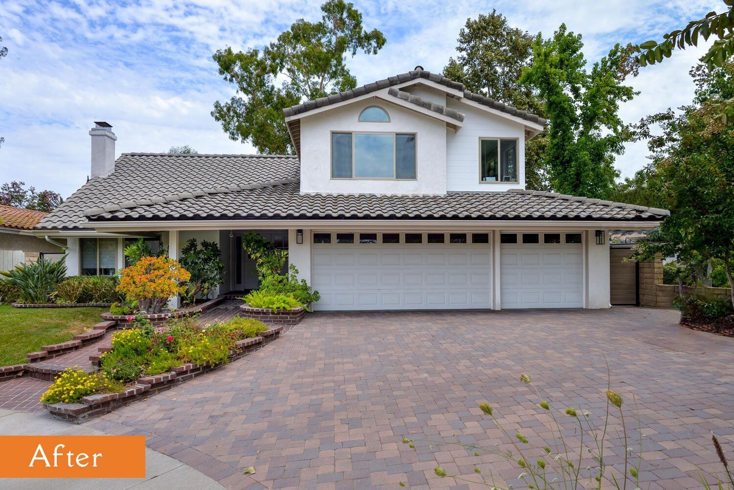 Suburban house with stone driveway, white garage, and landscaped front yard under a cloudy sky