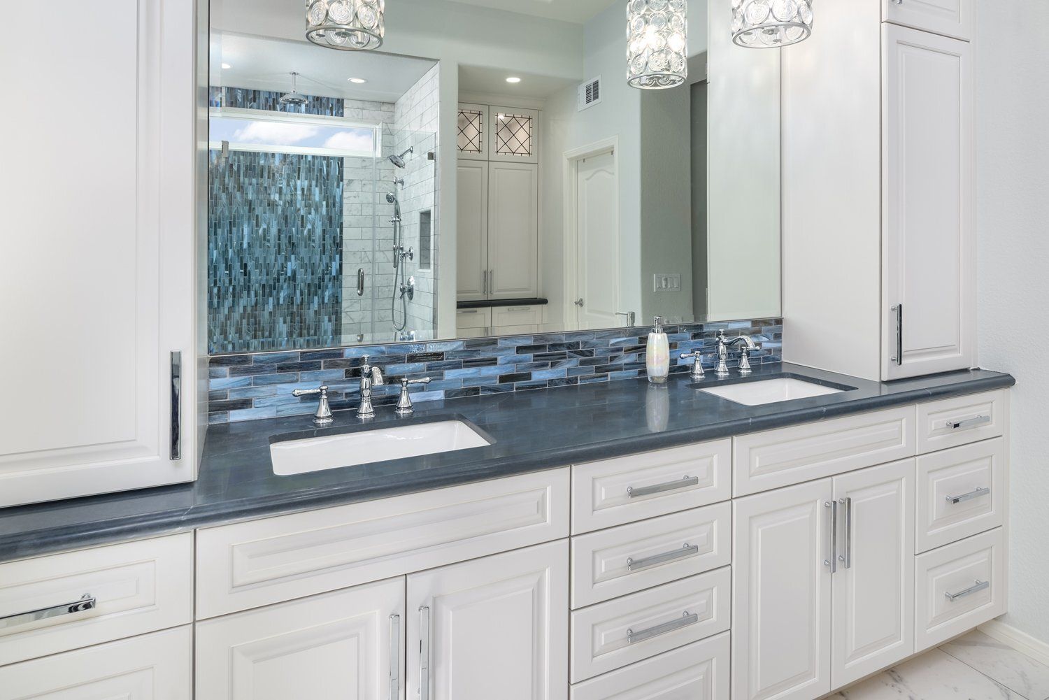 Modern white bathroom vanity with double sinks, black countertop, and large mirror beneath crystal light fixtures