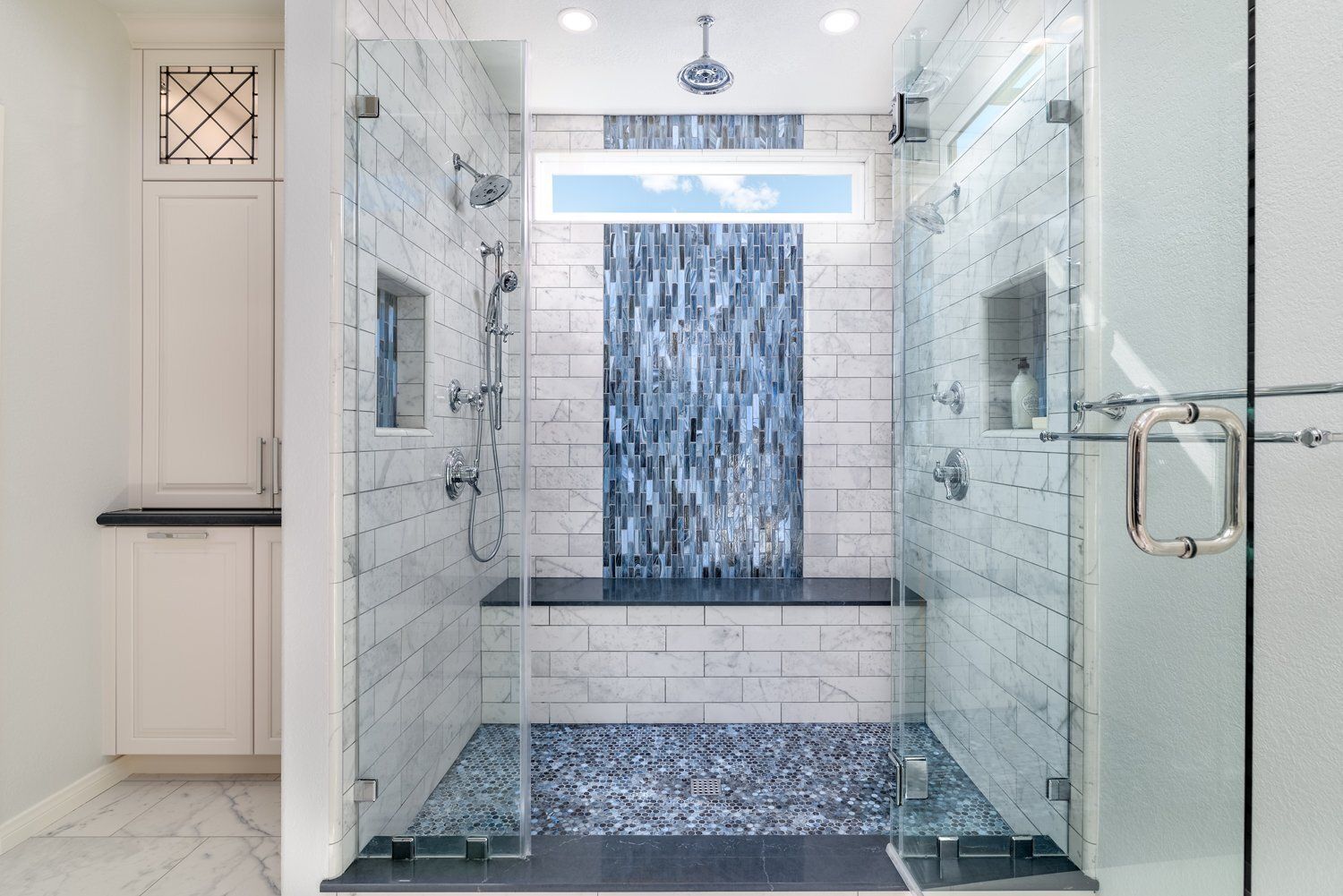 Modern glass shower with marble tile, blue mosaic accent wall, and frosted glass door in a bright bathroom