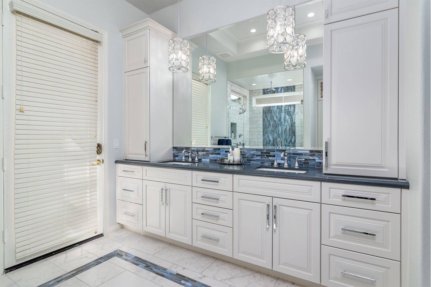 Bright white bathroom vanity with double sinks, dark countertops, mirrors, and crystal light fixtures