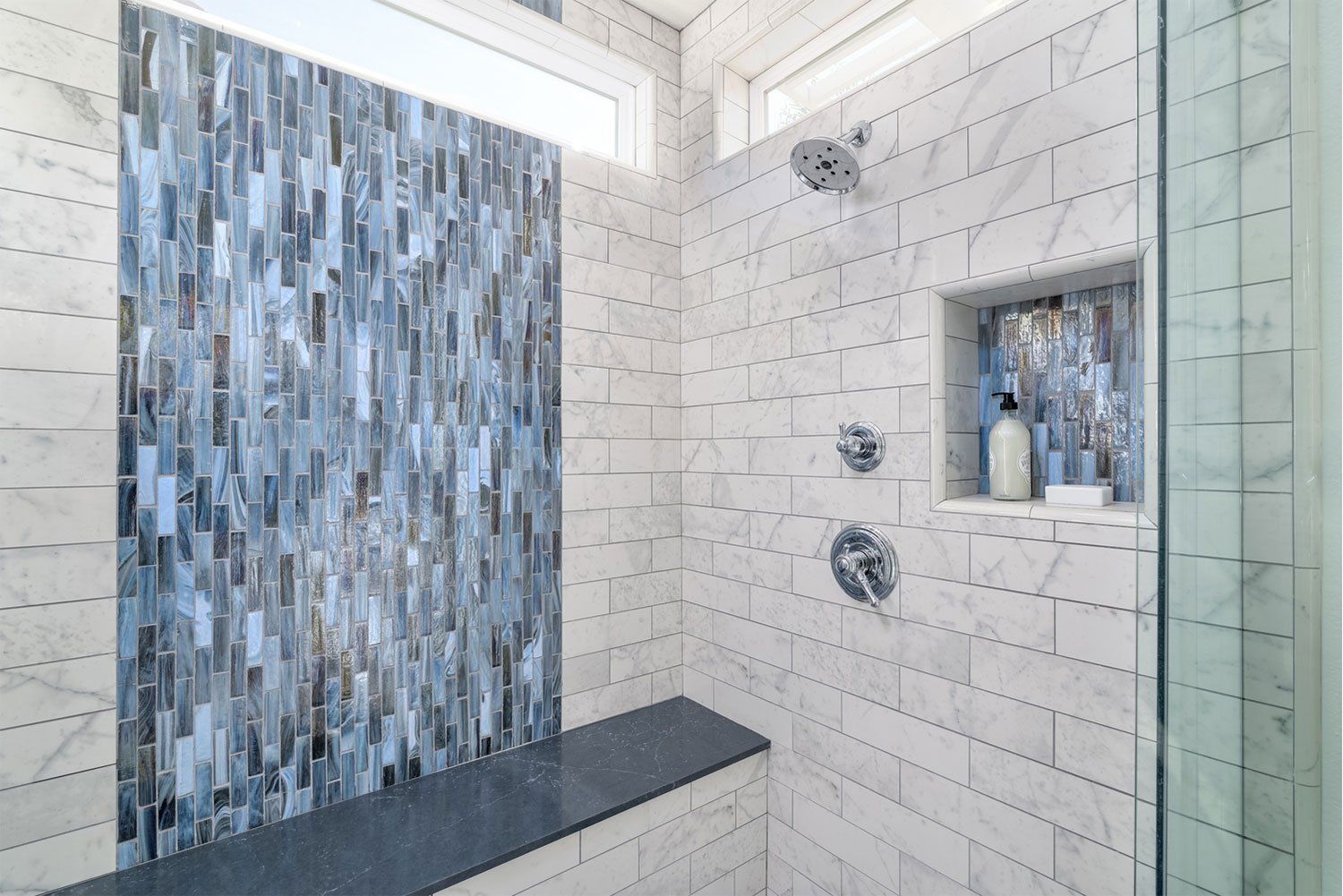 Modern bathroom shower with blue mosaic tile accent wall, white subway tiles, glass door, and built-in niche.