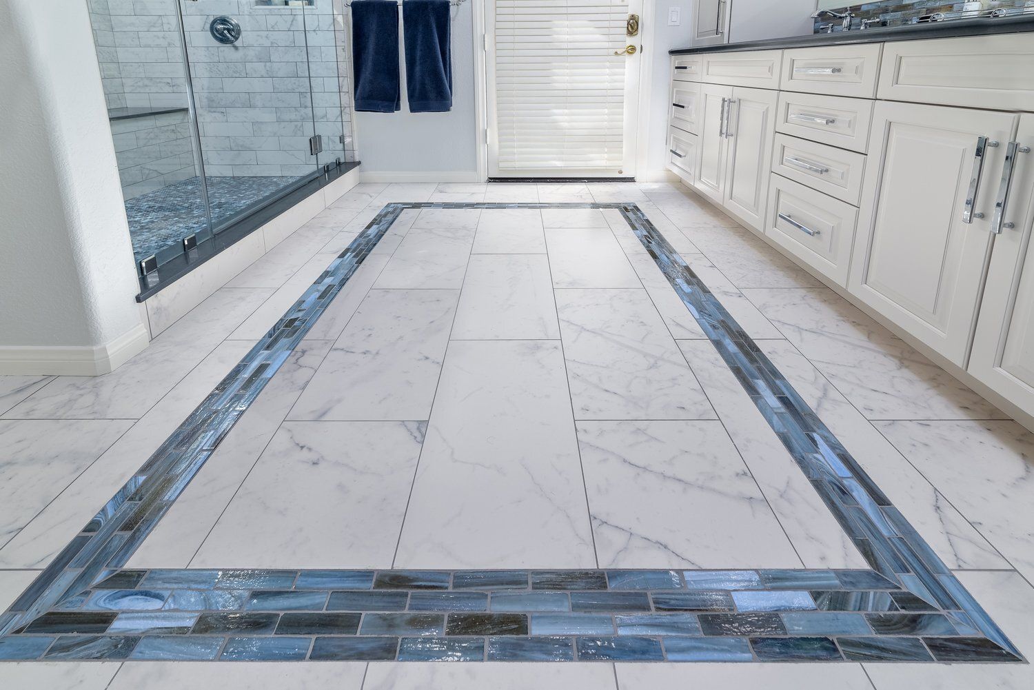 Empty kitchen floor with white tiles and blue-gray border trim leading to a back door.
