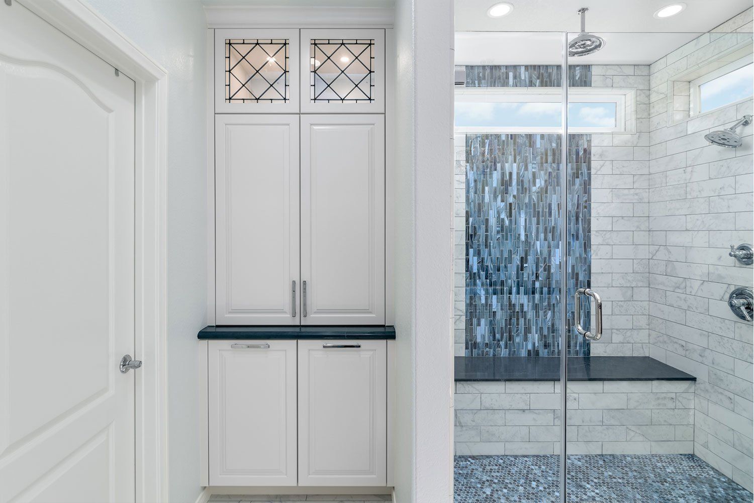 Bright white bathroom with built-in cabinets and a glass shower featuring blue tile accents