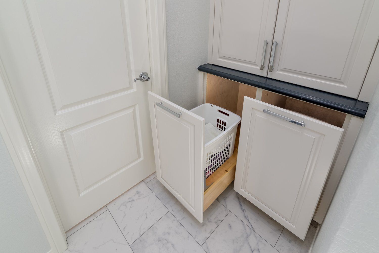 Laundry room with two white cabinets and a laundry hamper between them, one cabinet door open.