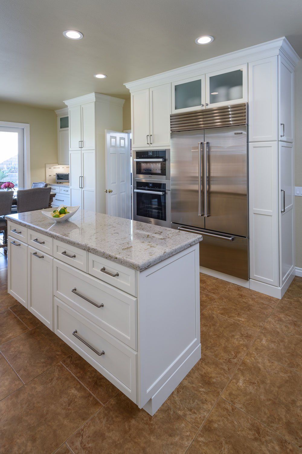 Bright modern kitchen with white cabinets, marble island, and stainless steel refrigerator and ovens