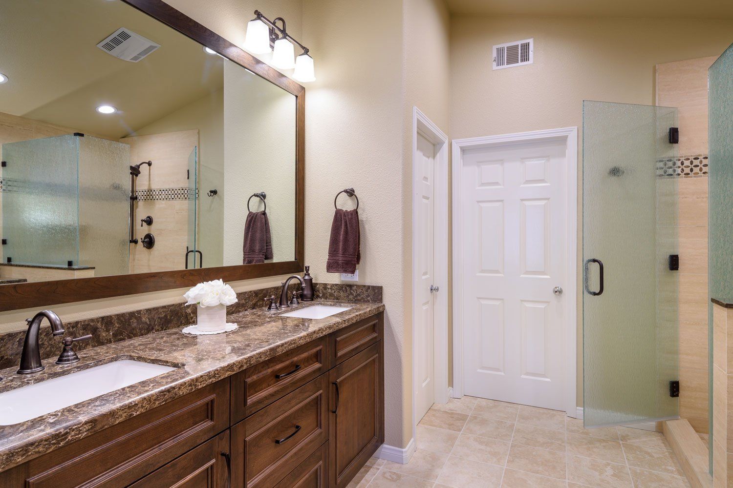 Spacious bathroom with double vanity, large mirror, glass shower, and frosted glass door