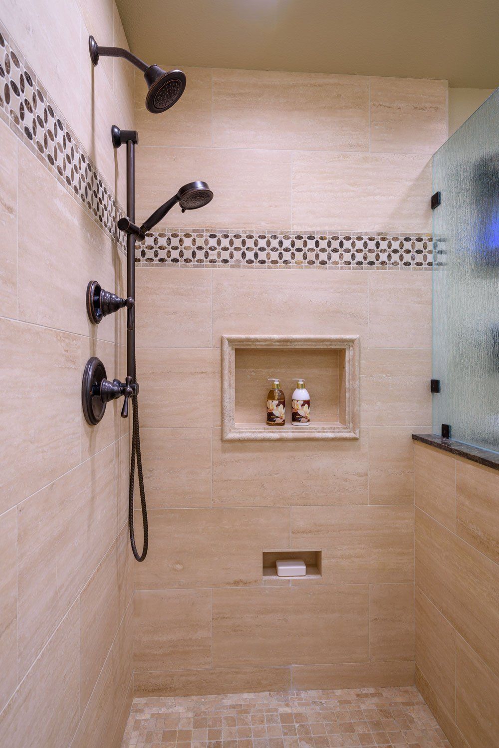 Tiled shower with glass wall, black fixtures, built-in shelf, and decorative border tile.