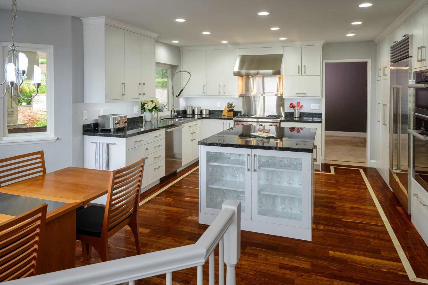 Bright modern kitchen with white cabinets, granite island, wooden floor, and dining table by a window.