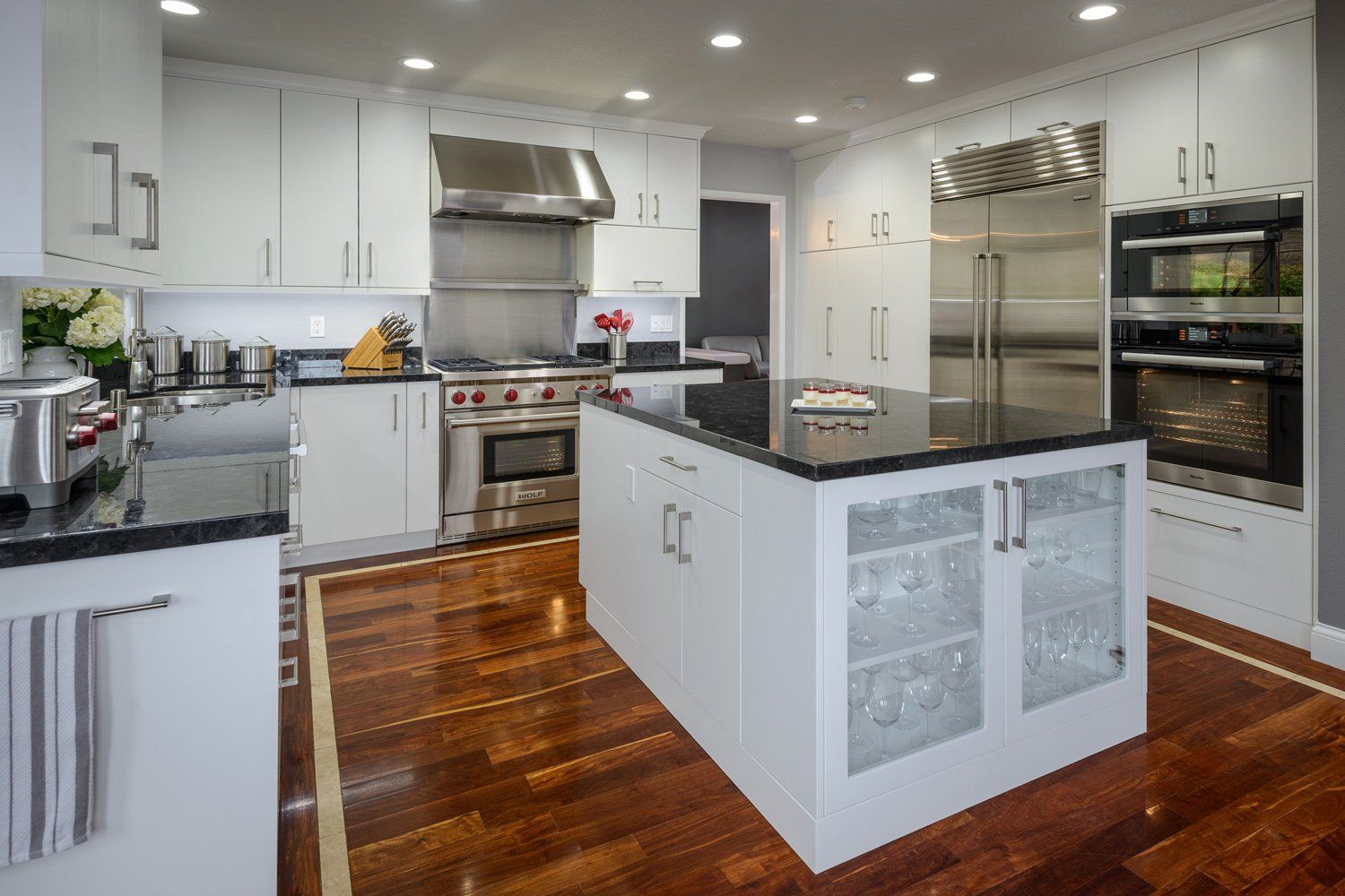 Bright white modern kitchen with island, stainless appliances, and polished wooden floors