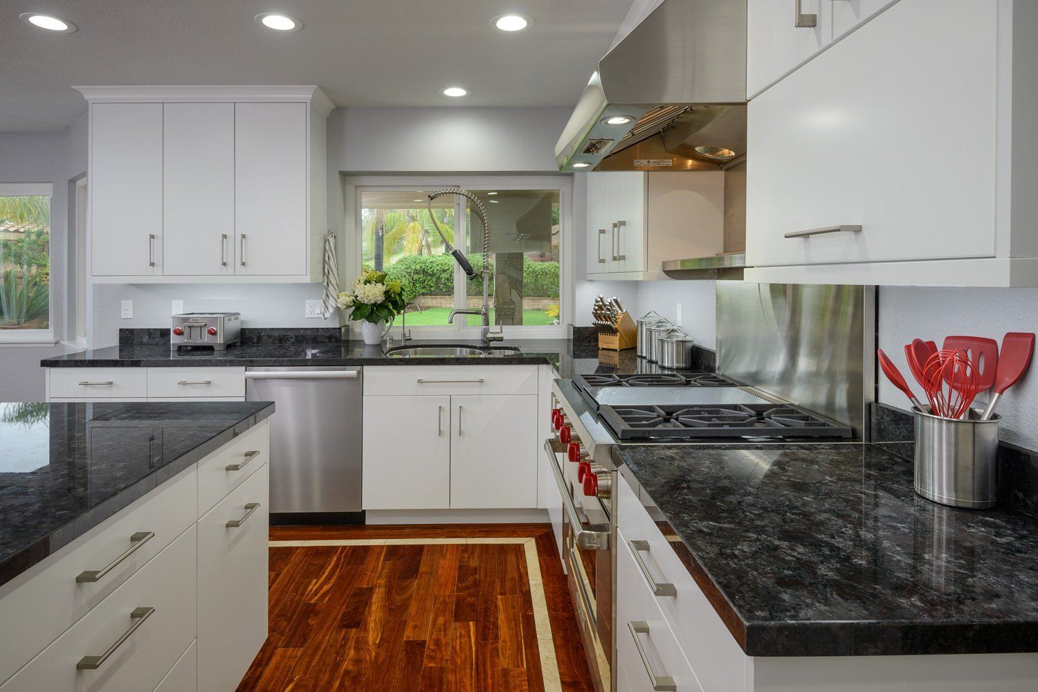 Bright modern kitchen with white cabinets, dark counters, stainless appliances, and a window over the sink.