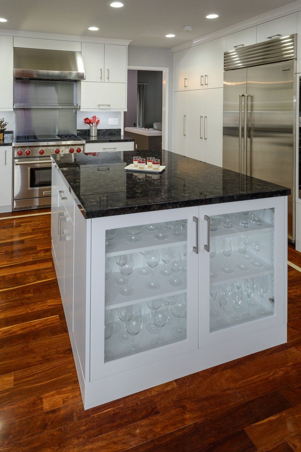 Modern kitchen with granite island, white cabinets, hardwood floors, and stainless steel appliances