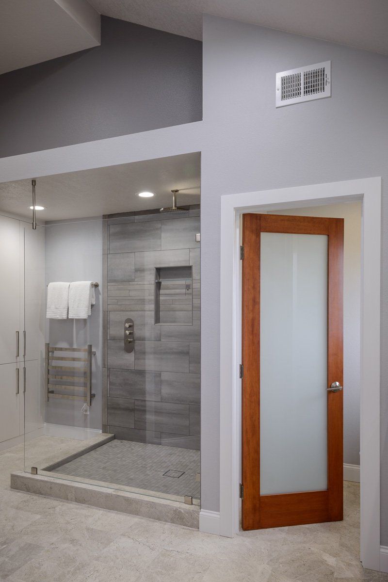 Modern bathroom with glass shower enclosure, gray tile walls, and a frosted wood-framed door.