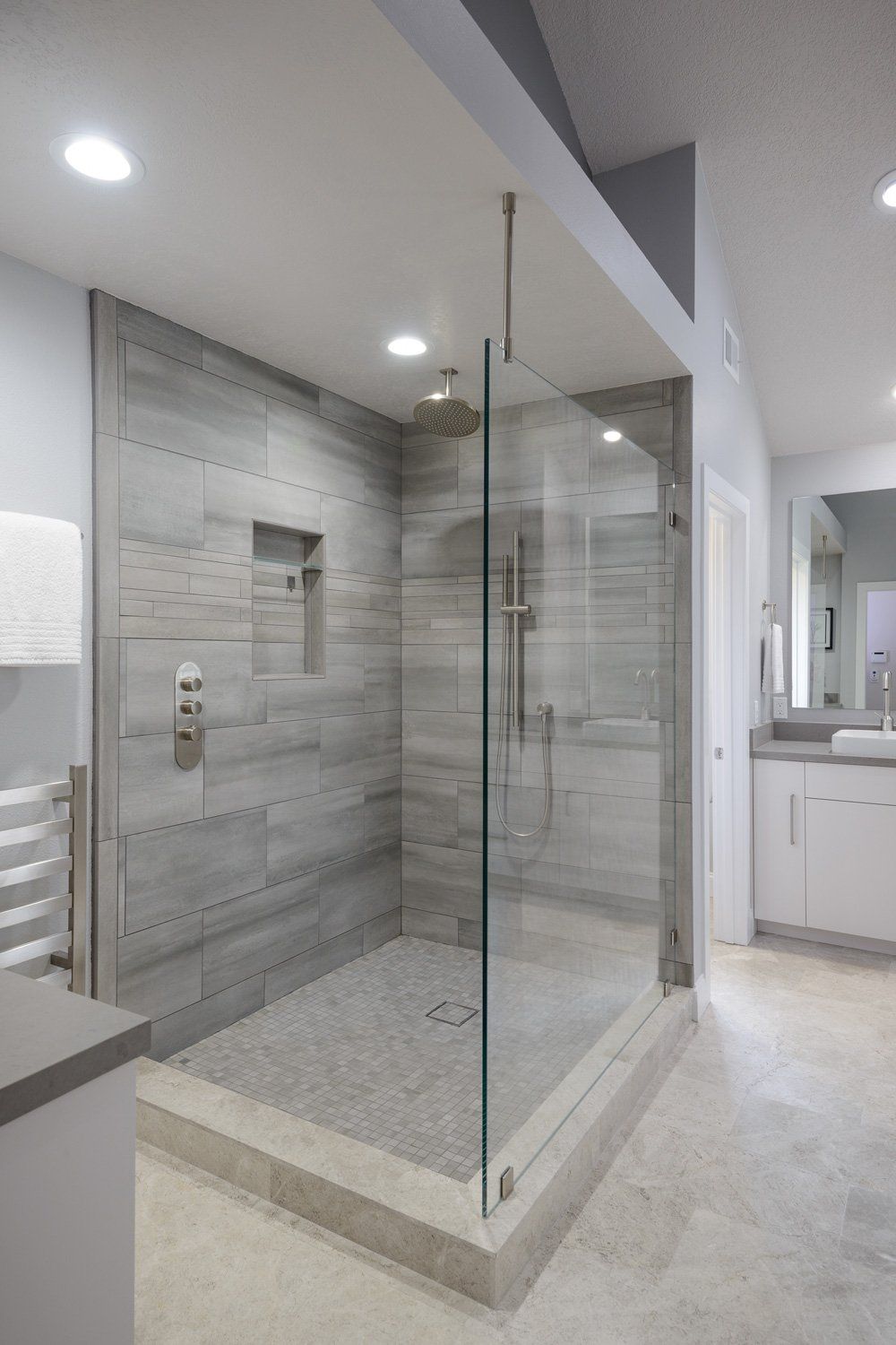Modern walk-in shower with glass enclosure, gray tile, and pebble shower floor in a bright bathroom