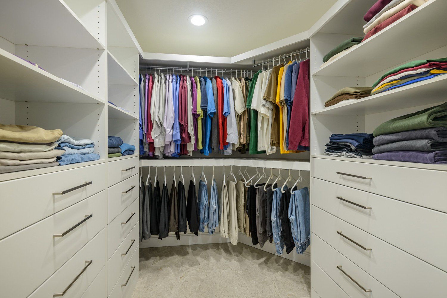 Walk-in closet with white shelves, drawers, and rows of neatly hanging clothes in various colors