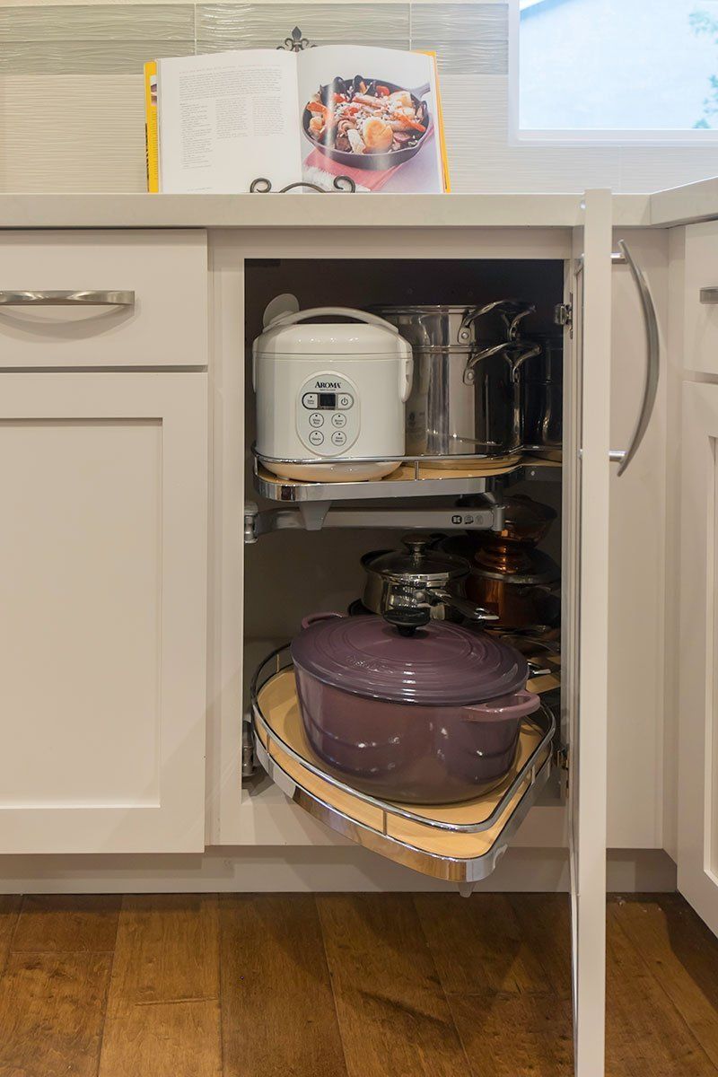 Open kitchen cabinet with cookware, including a purple pot, a white appliance, and stacked pots inside.