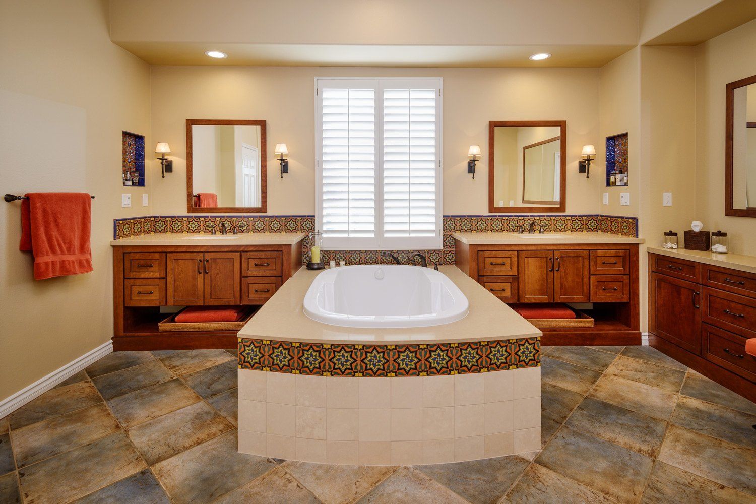 Spacious beige bathroom with a large white soaking tub, double vanity sinks, and patterned tile floor.