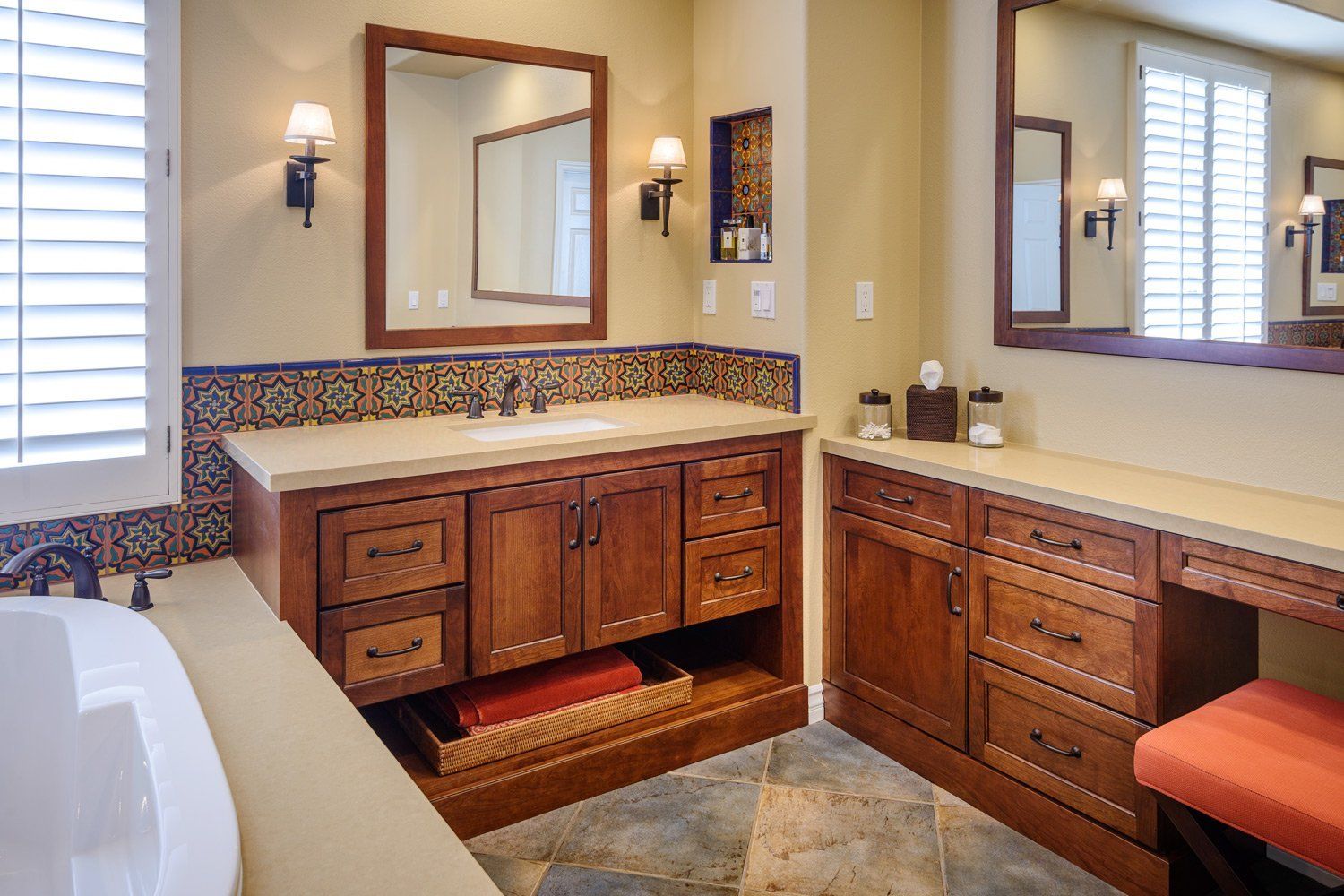 Bright bathroom with dual wood vanities, mirrors, stone countertop, and decorative tile backsplash