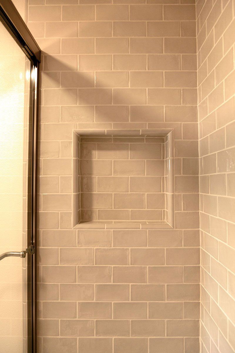 Tiled shower wall with a recessed soap niche and glass door edge on the left
