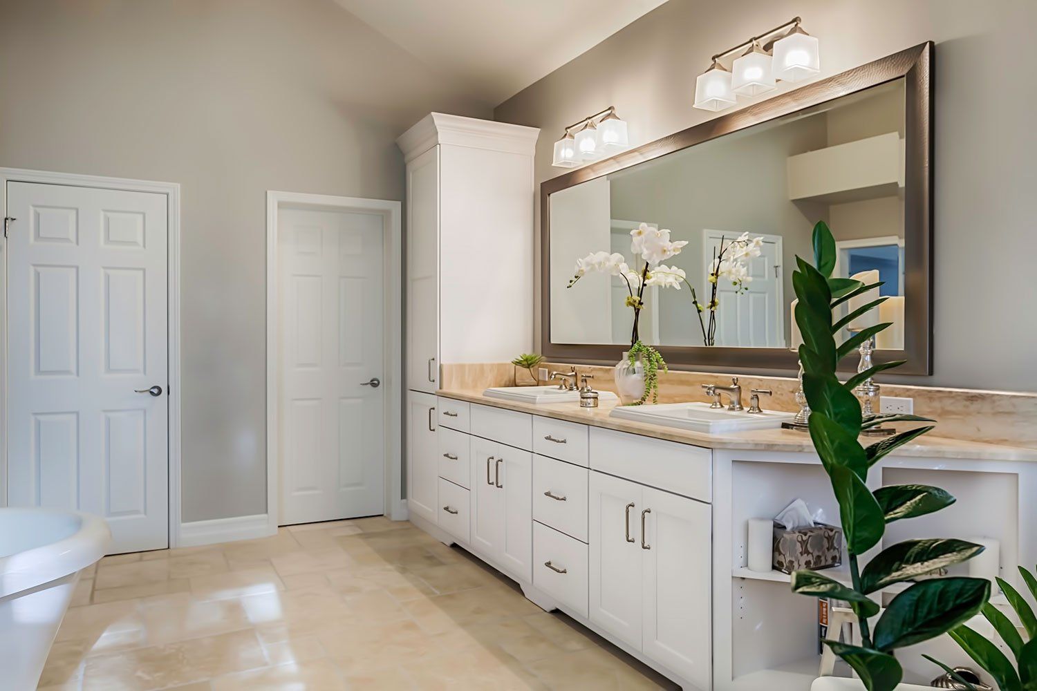Bright bathroom vanity with white cabinets, large mirror, beige countertop, and a potted plant.