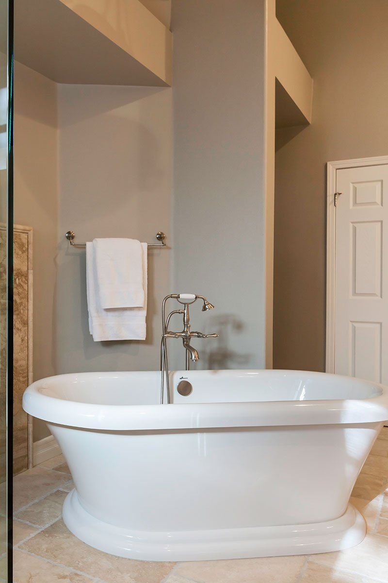 Freestanding white bathtub in a beige bathroom with towel rack and chrome fixtures