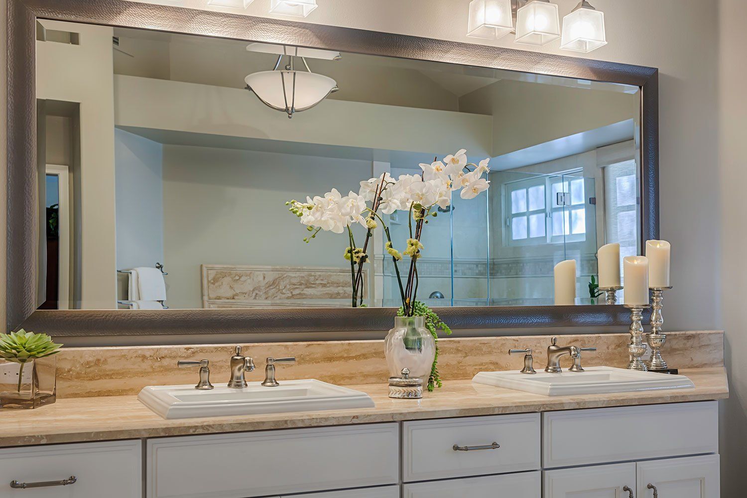 Bathroom vanity with large mirror, white sink, marble countertop, and vase of white flowers