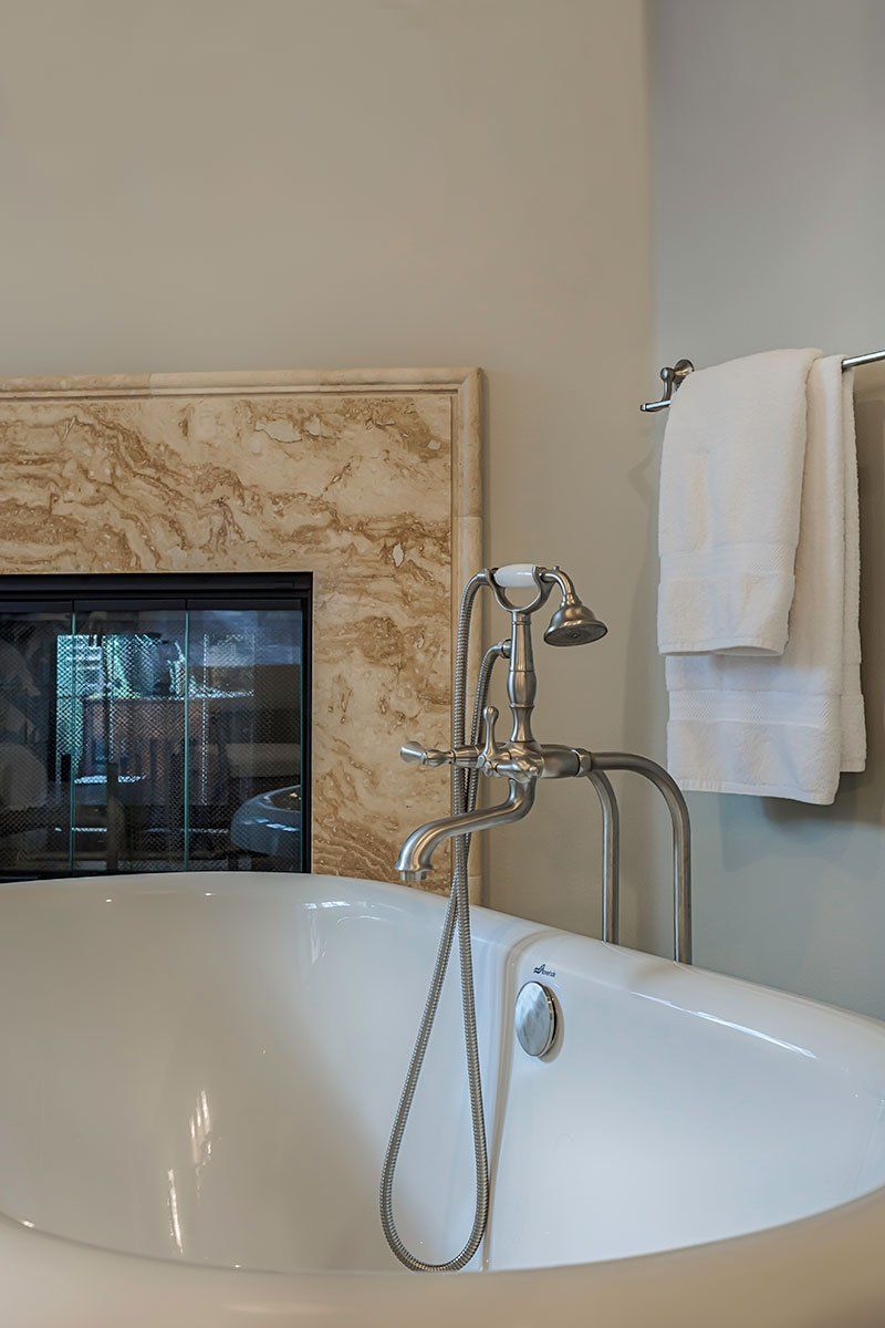 Bathroom tub with chrome faucet, beige marble surround, and white towels on a wall rack