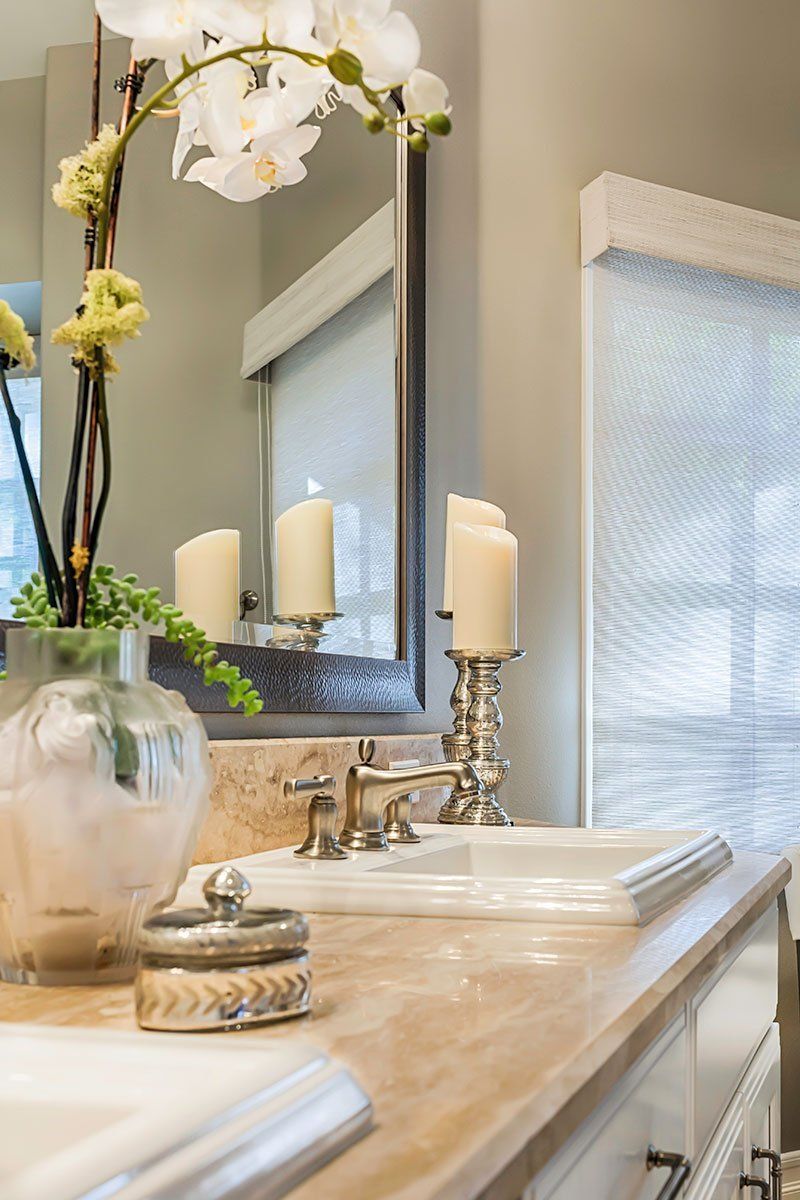 Elegant bathroom vanity with mirror, candles, flowers, and marble countertop near a window.