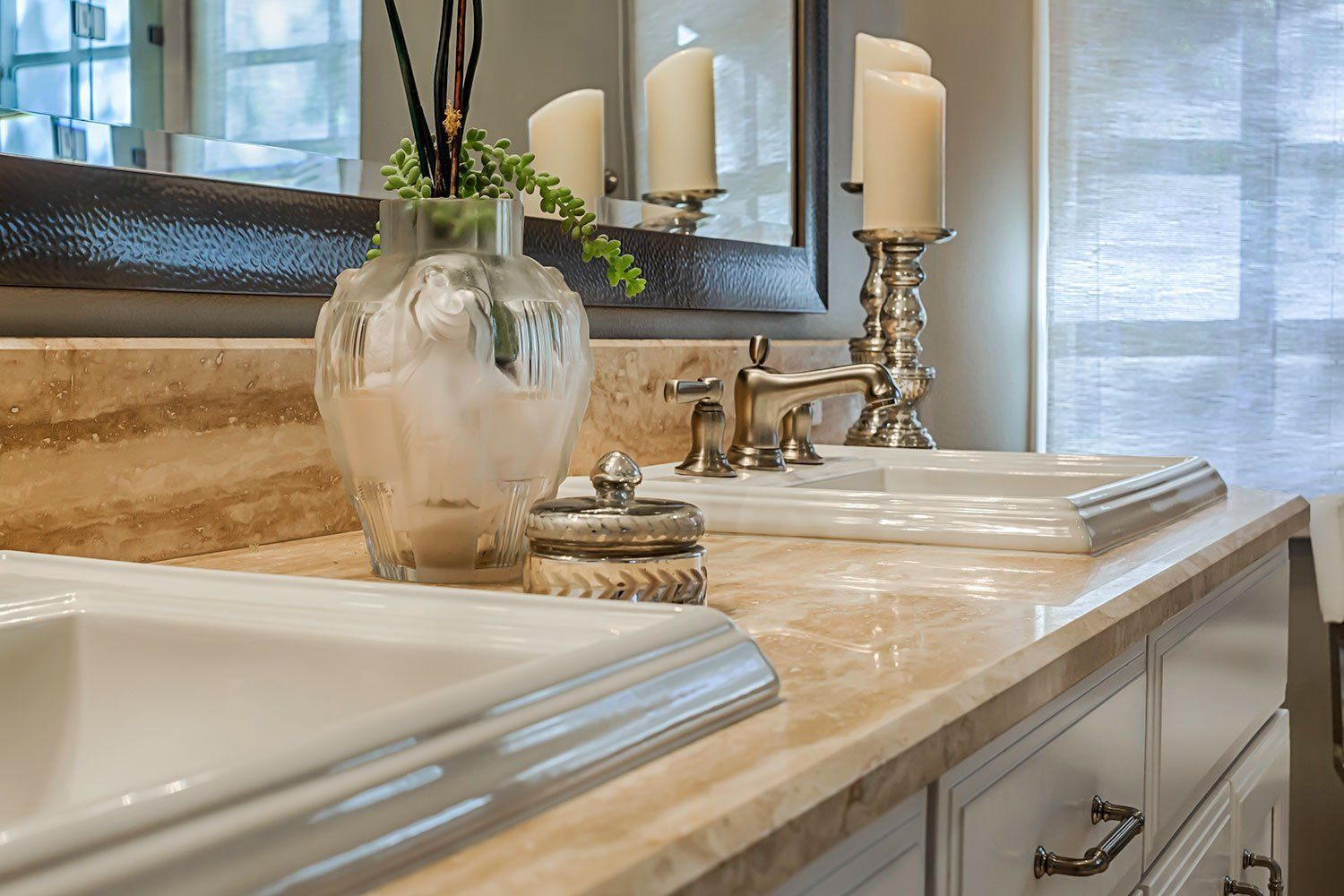 Bathroom vanity with double sinks, marble countertop, chrome faucets, and a vase of flowers near a mirror