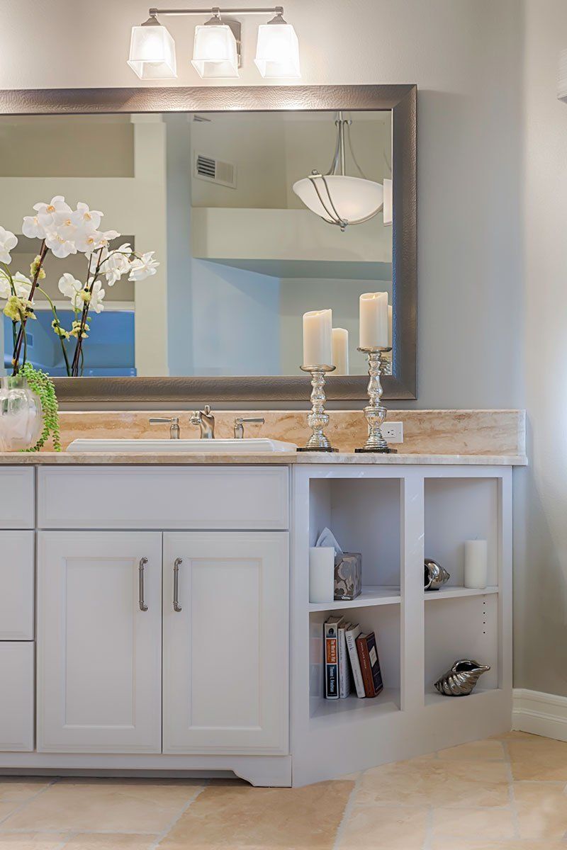 Bright bathroom vanity with mirror, white cabinets, candles, and orchid on the counter