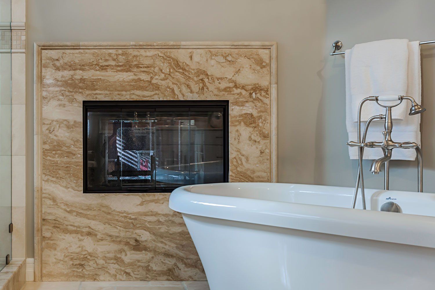Bathroom with marble fireplace, wall-mounted TV, and bathtub beside a towel rack