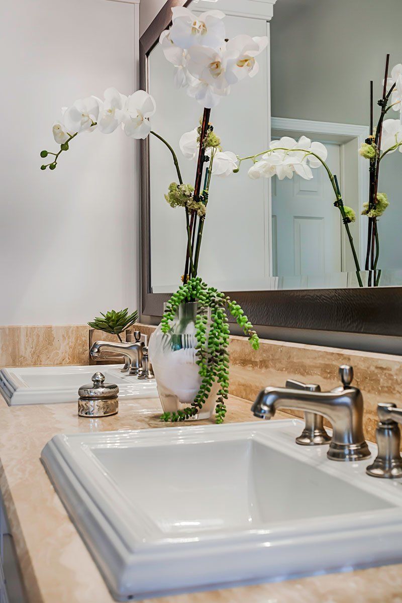 Bathroom sink with white orchid in vase beside mirror and chrome faucet