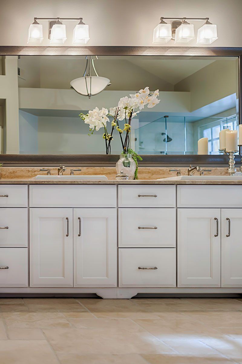Bright bathroom vanity with white cabinets, granite countertop, large mirror, and vase of white flowers