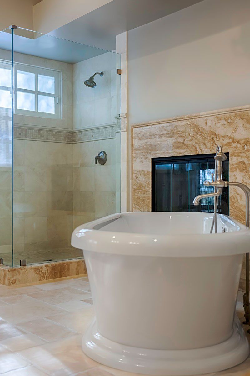Modern bathroom with glass shower, freestanding white tub, and beige tile fireplace niche