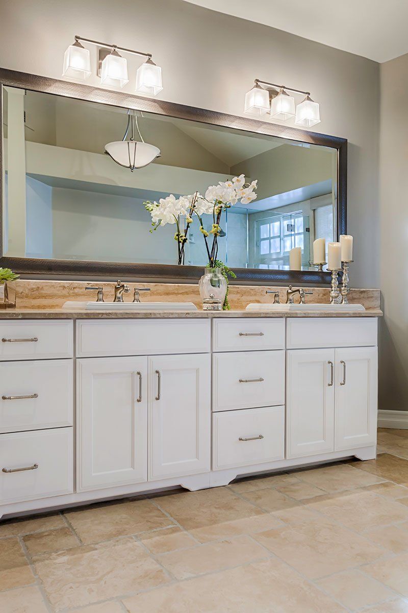 White bathroom vanity with double sinks, large mirror, and wall lights in a beige-tiled room