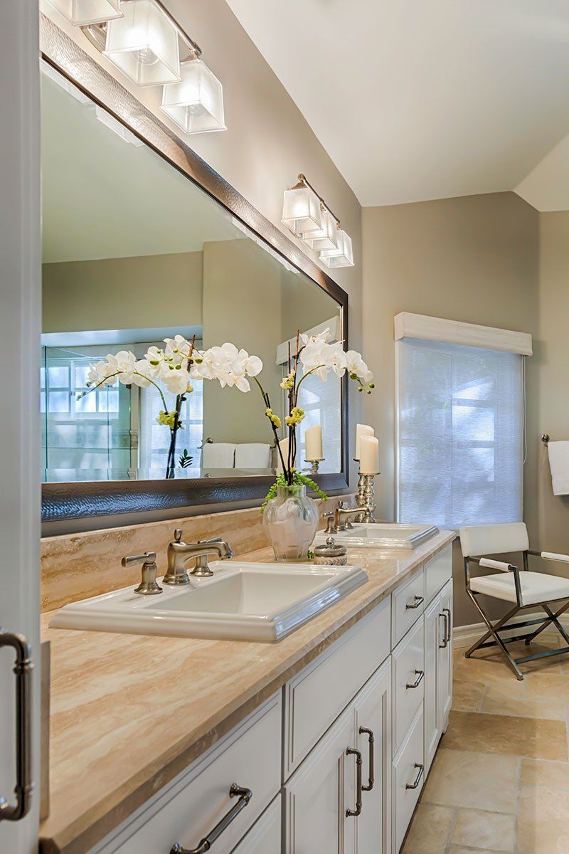 Modern bathroom vanity with mirror, white sink, wood countertop, orchids, and a chair by the window