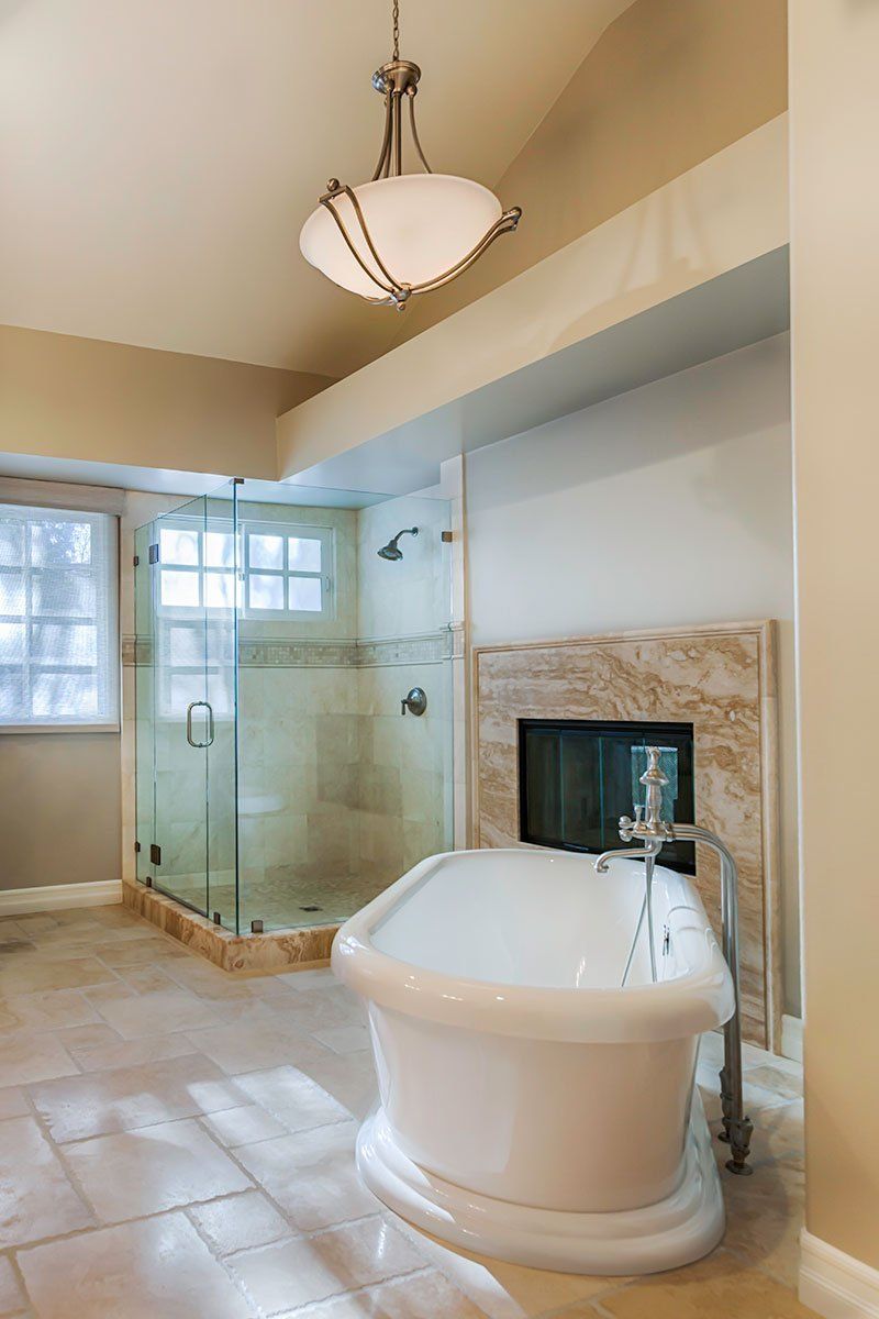 Spacious bathroom with a glass shower, freestanding tub, and tiled floor under a chandelier.