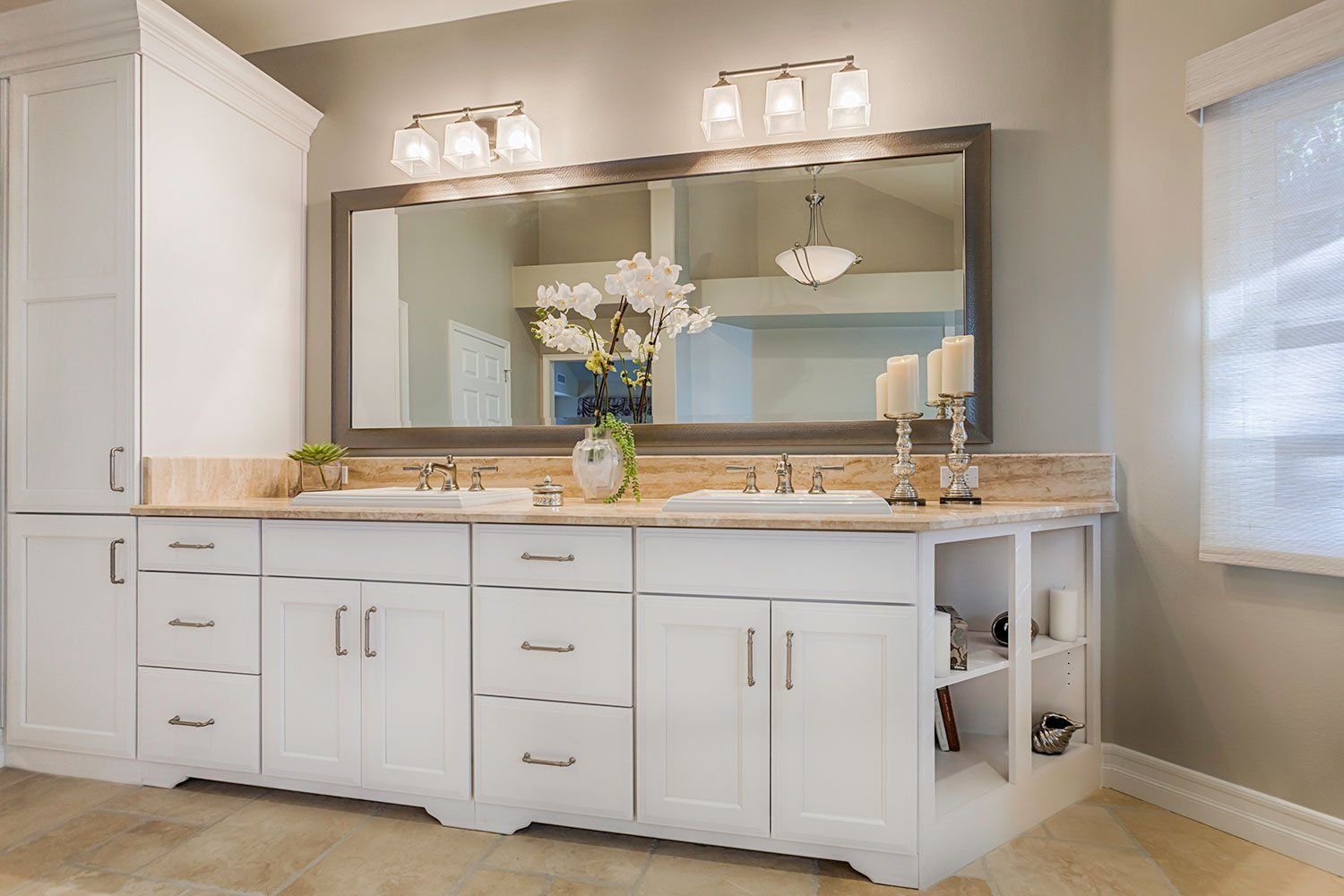 White bathroom vanity with double sinks, large mirror, and wall sconces in a bright neutral room
