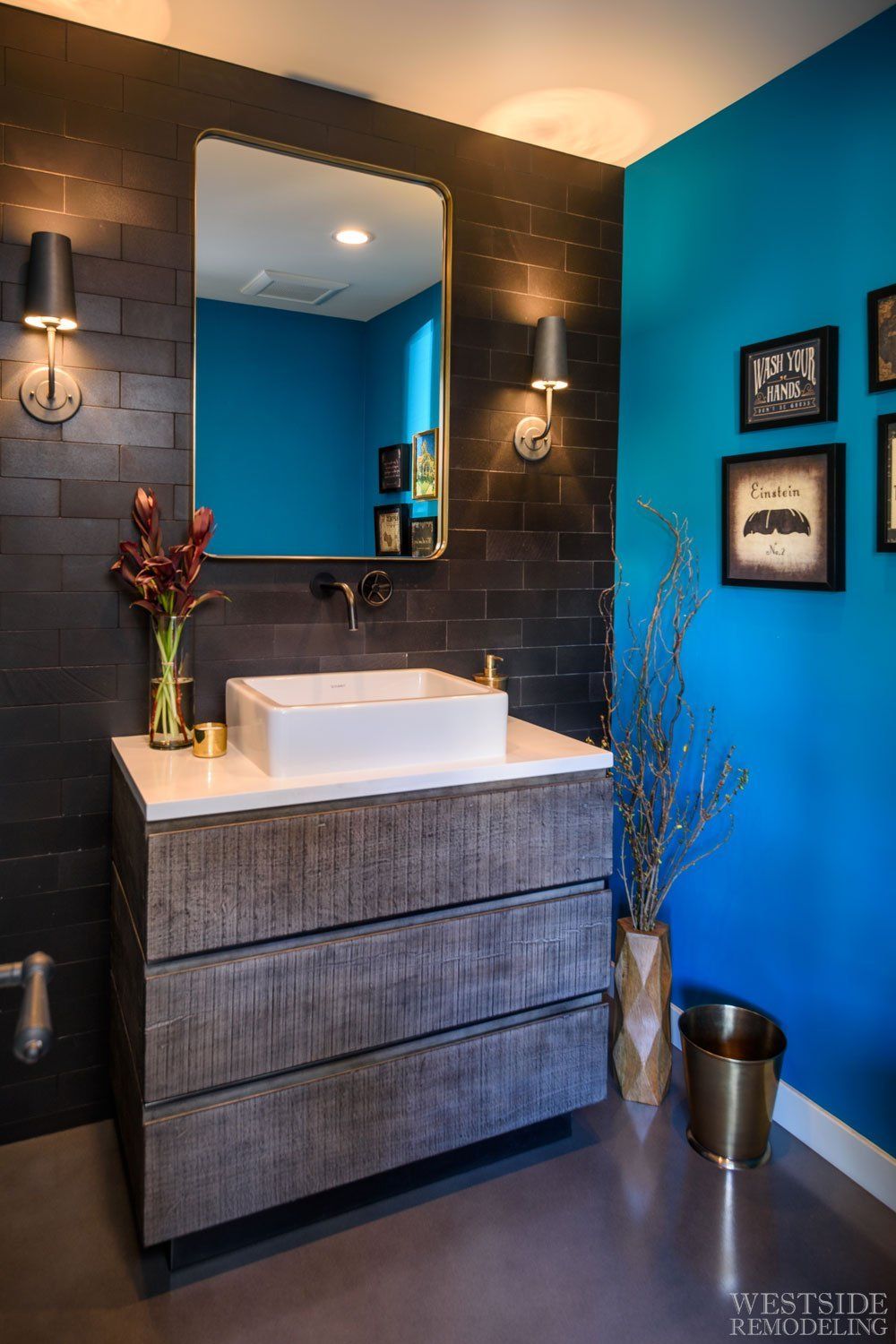 Modern bathroom vanity with blue walls, dark tile, square sink, mirror, and wall sconces.