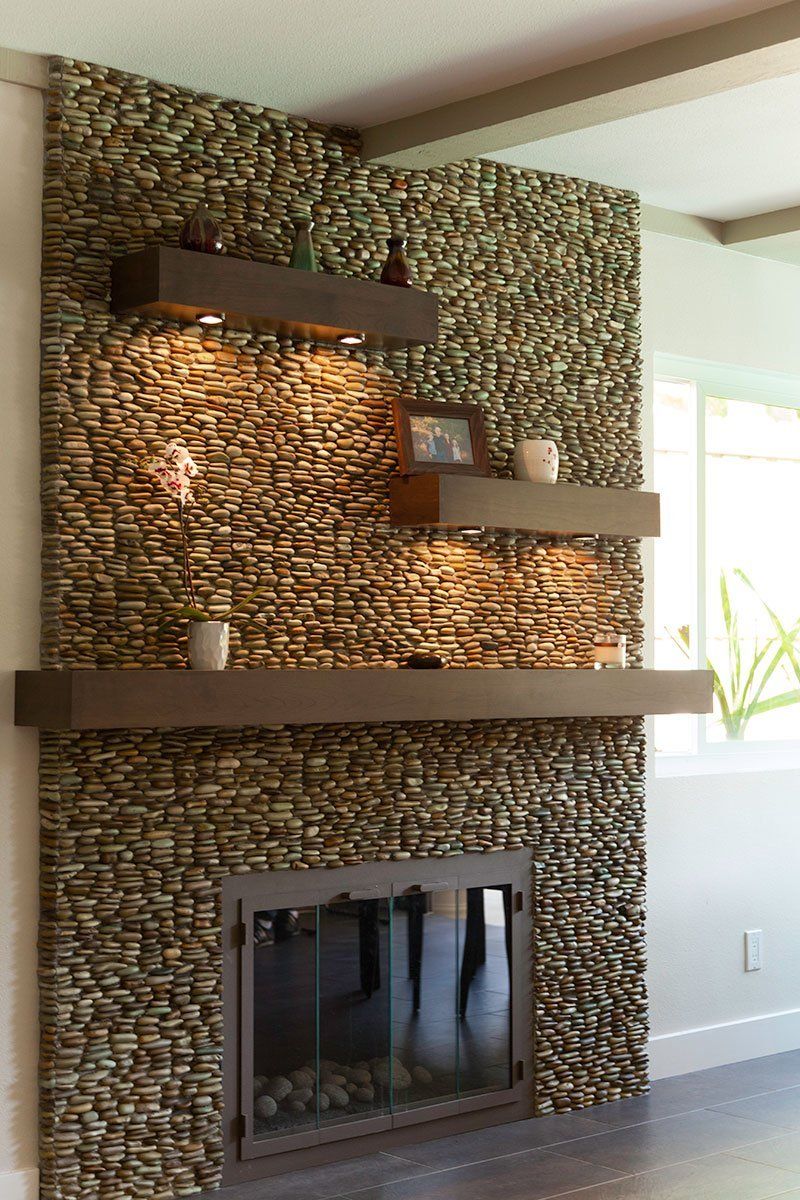 Modern living room fireplace with stacked stone surround, floating shelves, and daylight from a window