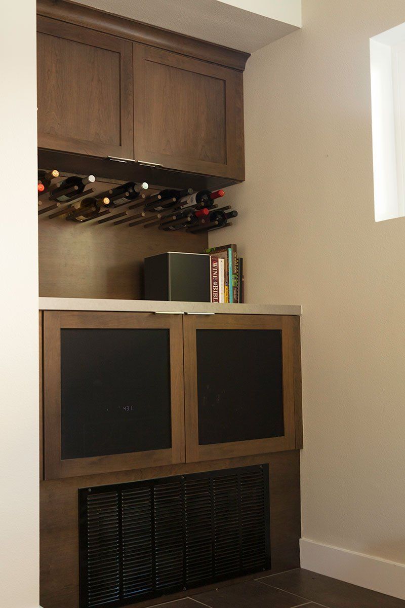 Small wooden cabinet with two black front panels beneath a wine rack in a kitchen nook.