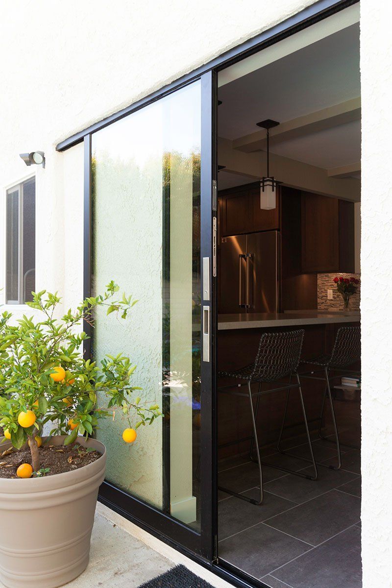Sliding glass doors open to a modern patio and kitchen, with a potted lemon tree by the wall.