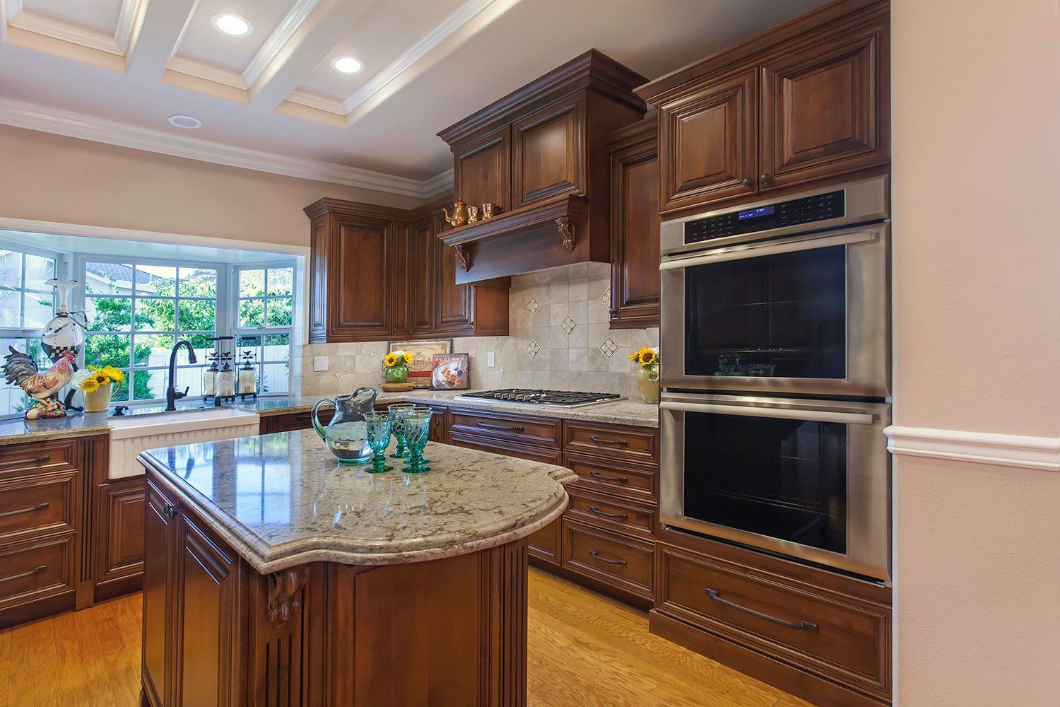 Elegant kitchen with wood cabinets, granite island, double ovens, and large window above the sink.