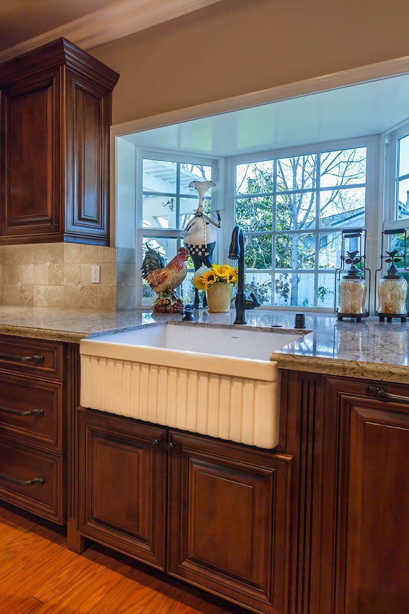 Warm kitchen with dark wood cabinets, beige countertops, and a large window over a farmhouse sink.