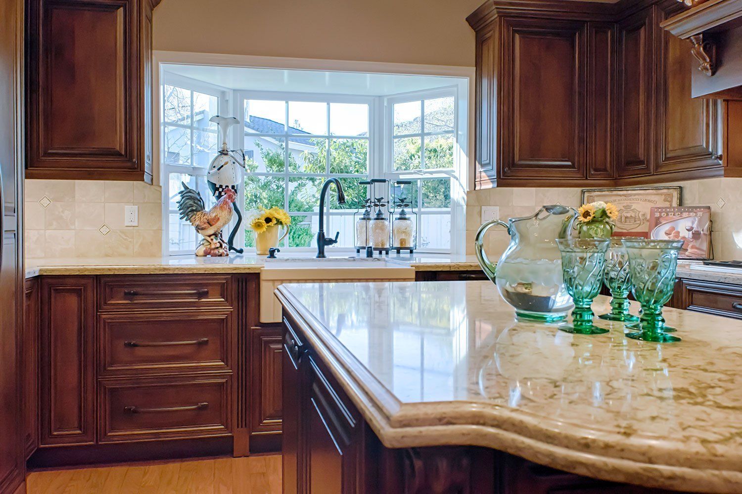 Bright kitchen with wooden cabinets, granite island, and bay window above the sink with decorative glass vases